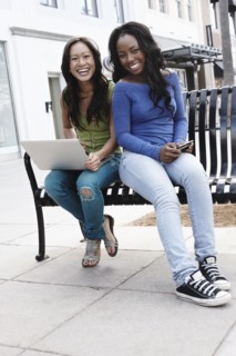 Friends sitting on bench using laptop