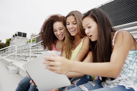 School friends sitting together on bleachers using digital tablet