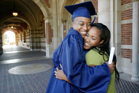 Smiling Black woman holding graduation diploma and hugging daughter