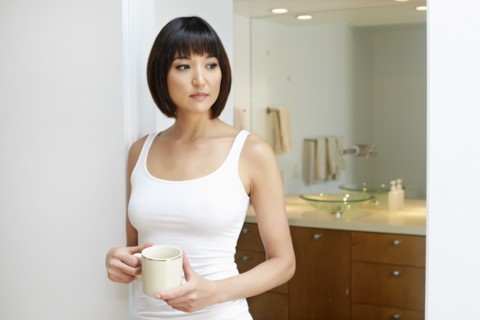 Mixed race woman holding cup in bathroom