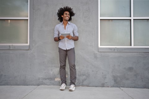 Man using digital tablet and leaning on wall outdoors