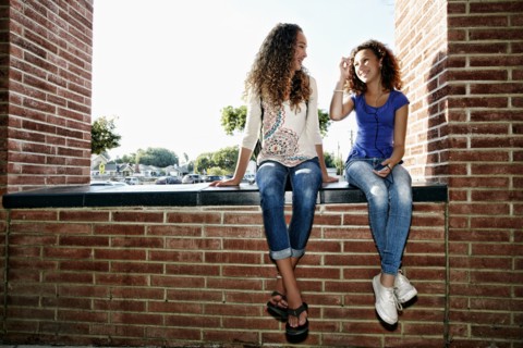 Mixed race girls sitting on brick ledge
