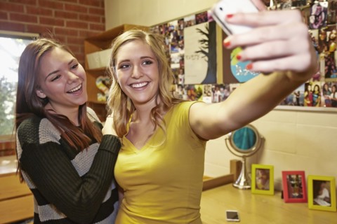 Caucasian students taking pictures in dorm room