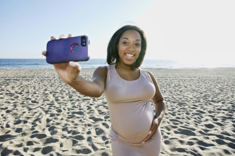 Pregnant woman taking cell phone picture on beach