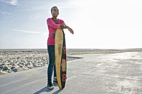 Older Black woman holding skateboard on beach