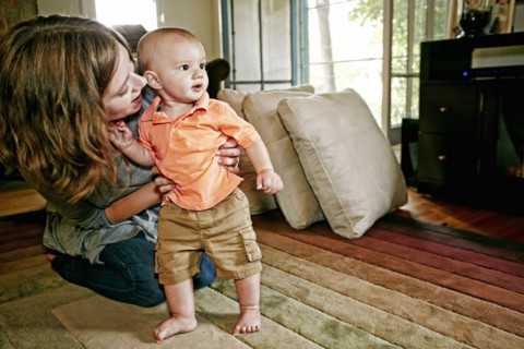 Caucasian mother helping baby walk on living room floor