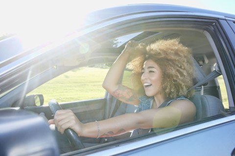Hispanic woman cheering and driving car