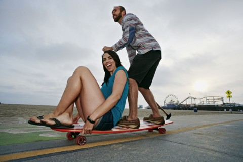 Caucasian couple skateboarding with paddle pole at beach