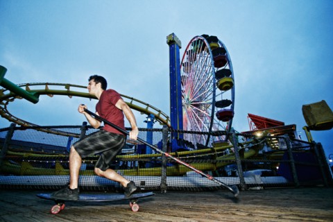 Caucasian man skateboarding with paddle pole at amusement park