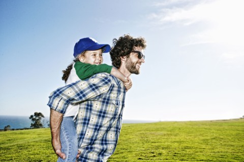 Father carrying daughter piggyback in grassy field
