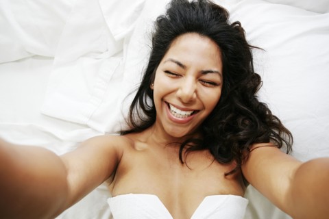 Hispanic woman taking selfie of herself on bed