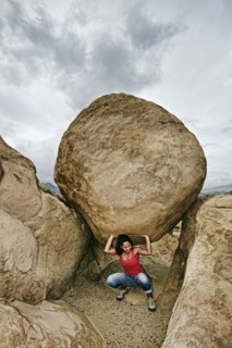 Hispanic woman lifting boulder on rocky hillside