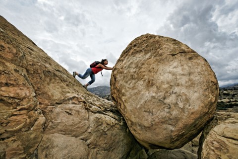 Hispanic woman pushing boulder on rocky hillside