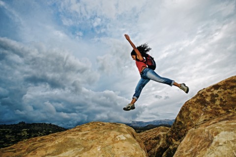 Hispanic woman jumping crevasse on rock formation