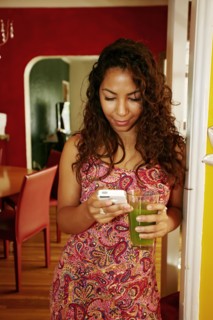 Hispanic woman drinking green juice and using cell phone