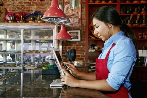 Hispanic cashier using digital tablet register in bakery