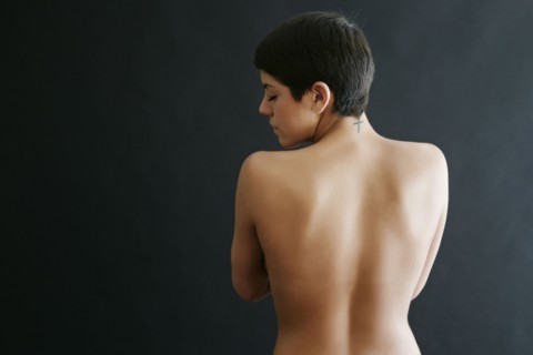 Rear view of nude Hispanic woman with tattoo on neck