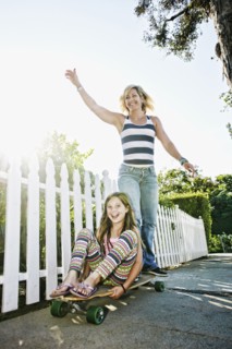 Caucasian mother and daughter riding skateboard on sidewalk