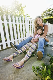 Caucasian mother and daughter riding skateboard on sidewalk