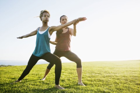 Teacher helping student practice yoga outdoors