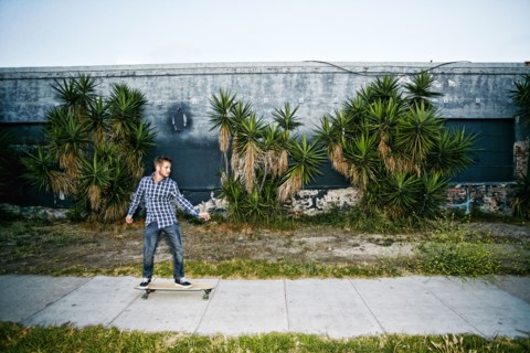Caucasian man riding skateboard on sidewalk