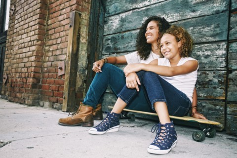 Mixed race mother and daughter sitting on skateboard