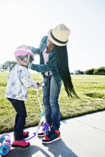 Black mother fastening helmet on daughter
