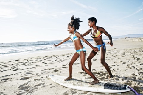 Black mother teaching daughter to surf on beach