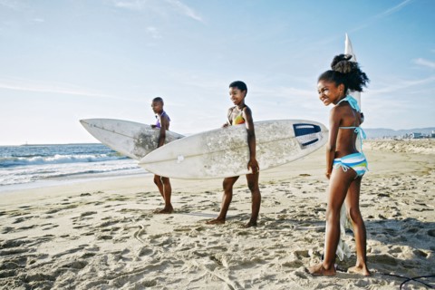 Three generations of Black women carrying surfboards on beach