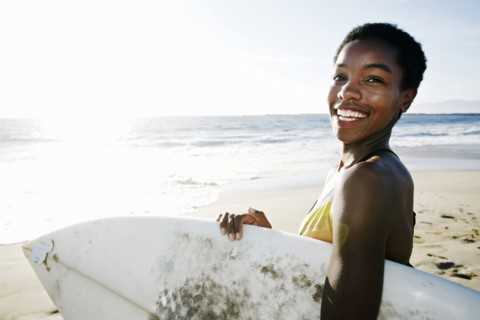Black woman carrying surfboard on beach