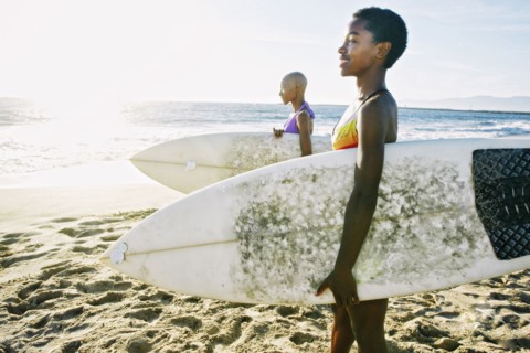 Black women carrying surfboards on beach