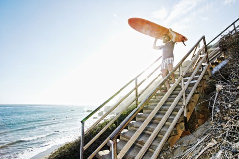 Caucasian man carrying surfboard on stairs at beach