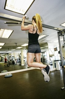 Pacific Islander woman doing pull-ups in gymnasium