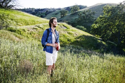 Caucasian hiker standing in grass on mountain holding water bottle