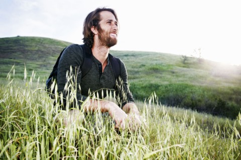 Caucasian hiker crouching in grass on mountain