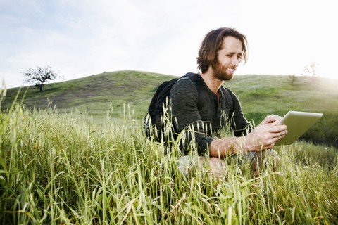 Caucasian hiker crouching in grass on mountain using digital tablet