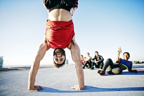Woman photographing man doing handstand on urban rooftop