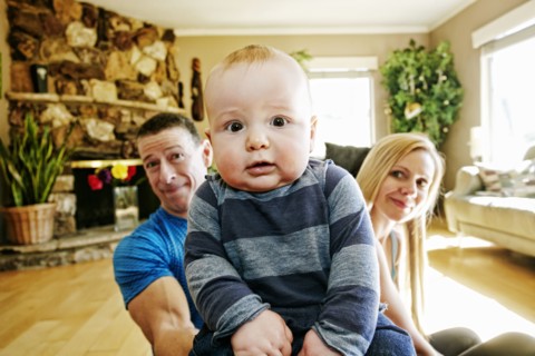 Mother and father posing behind baby on livingroom floor