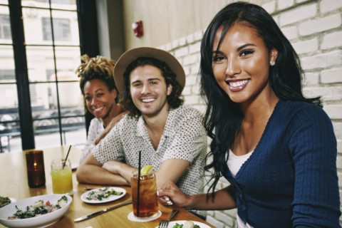 Smiling friends enjoying food and cocktails at table in bar