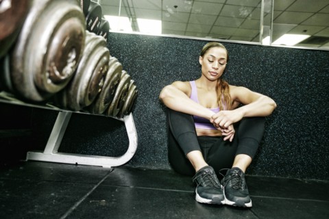 Mixed Race woman sitting on floor resting in gymnasium