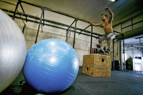 Caucasian man jumping on wooden crate in gymnasium