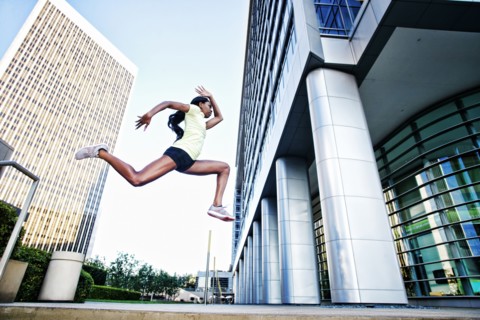 Black woman running and jumping on city sidewalk