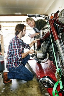 Caucasian father watching son repairing motorcycle in garage