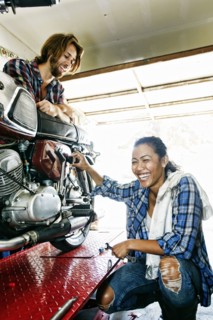 Man watching laughing woman repairing motorcycle in garage