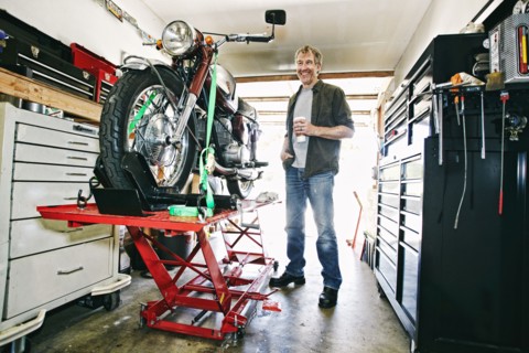 Caucasian man drinking coffee while repairing motorcycle in garage