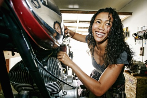 Laughing Mixed Race woman repairing motorcycle in garage