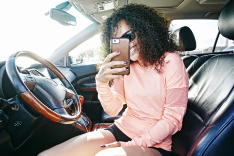 Smiling Hispanic woman in car posing for cell phone selfie
