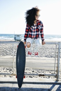 Hispanic woman sitting on fence at beach with skateboard