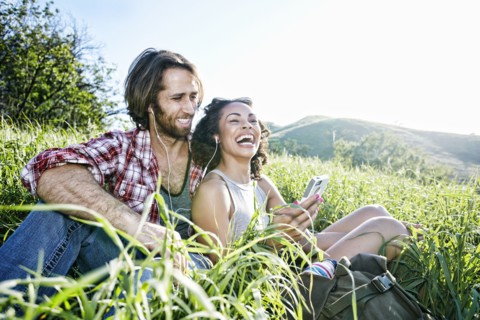 Smiling couple sitting on hill listening to cell phone