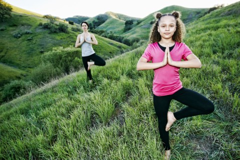 Mother and daughter practicing yoga on hill